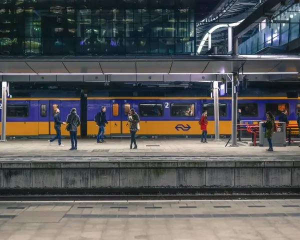 Ludzie na peronie czekają na niebiesko-żółty pociąg na nowoczesnej stacji kolejowej.