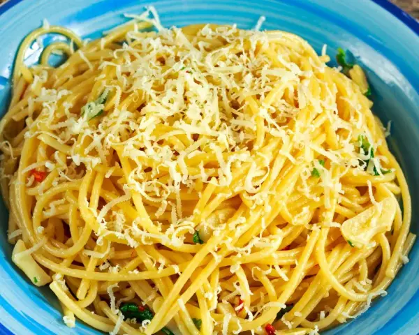 Porcja spaghetti z tartym serem i ziołami w niebieskiej misce.