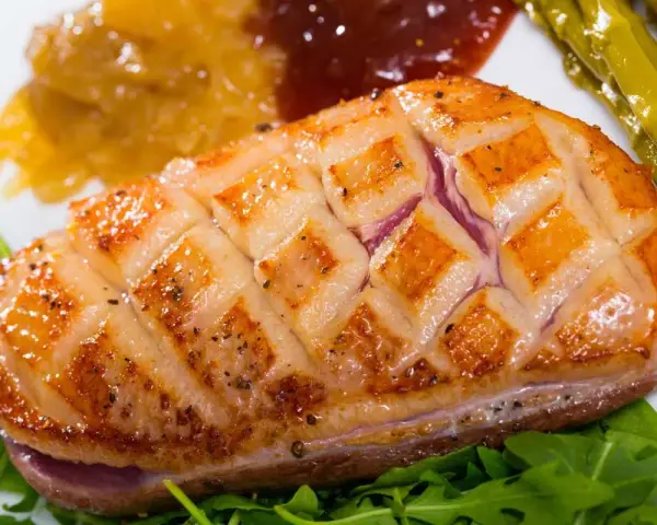Magret de pato perfectamente cocinado, con piel crujiente y jugoso por dentro, acompañado de espárragos y compota.