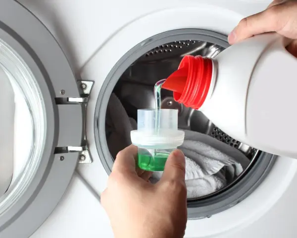 Versando detersivo liquido in un misurino per lavatrice. Ideale per capi delicati, cosa lavare a 20 gradi per preservare i colori.