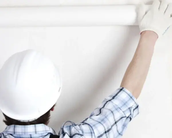 Un ouvrier en casque blanc déroule une **pose toile de verre** sur un mur blanc.