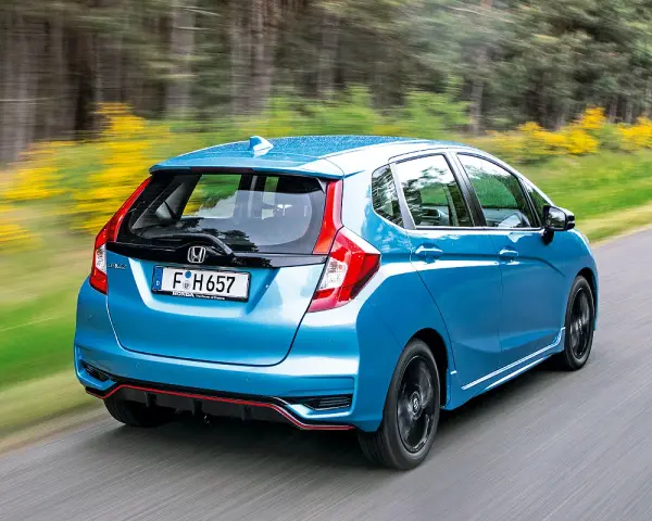 Blauer Honda Jazz Hybrid fährt auf einer Landstraße. Trotz der schönen Fahrt gibt es Berichte über Honda Jazz Hybrid Probleme.