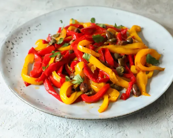 Peperoni in padella, tagliati a listarelle rosse e gialle, conditi con olive e capperi, guarniti con prezzemolo fresco.