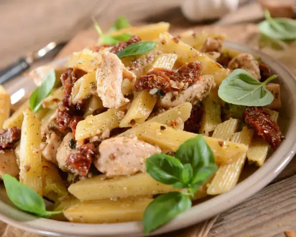 Penne z kurczakiem i suszonymi pomidorami, ozdobione świeżą bazylią. Pyszne danie na obiad.