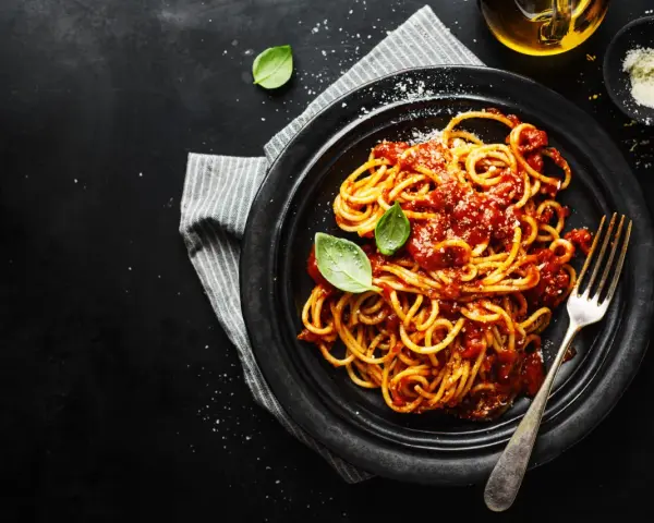 Un piatto di spaghetti alla carrettiera fumanti, conditi con un ricco sugo di pomodoro e basilico fresco, su sfondo scuro.