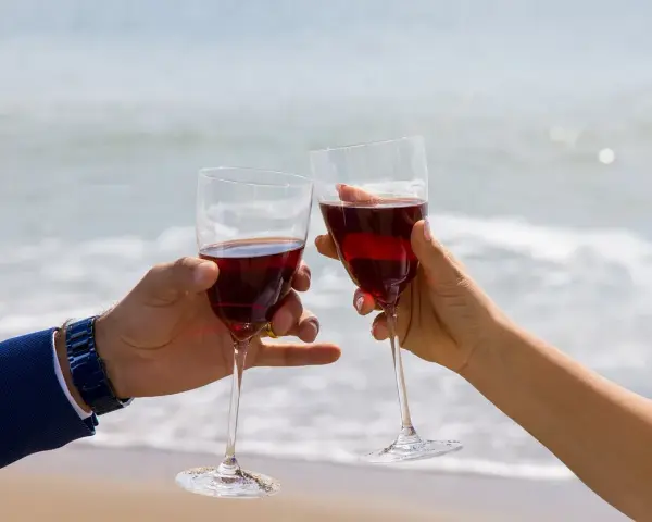 Dwie ręce unoszą kieliszki z czerwonym winem na tle morza. Idealne drinki z winem na romantyczny wieczór.