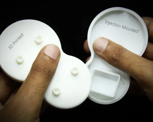 Hands hold two white plastic parts, one labeled "3D Printed" and the other "Injection Moulded," showcasing the difference between the two manufacturing methods.