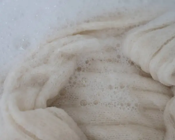 Lana bianca in acqua saponata, un processo che porta all'infeltrimento della lana per creare texture uniche.