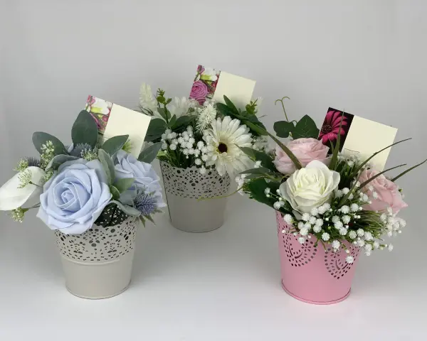 Inspiracje, jak udekorować kwiaty doniczkowe na prezent: trzy urocze bukieciki w ozdobnych doniczkach, każdy z kartką na życzenia.