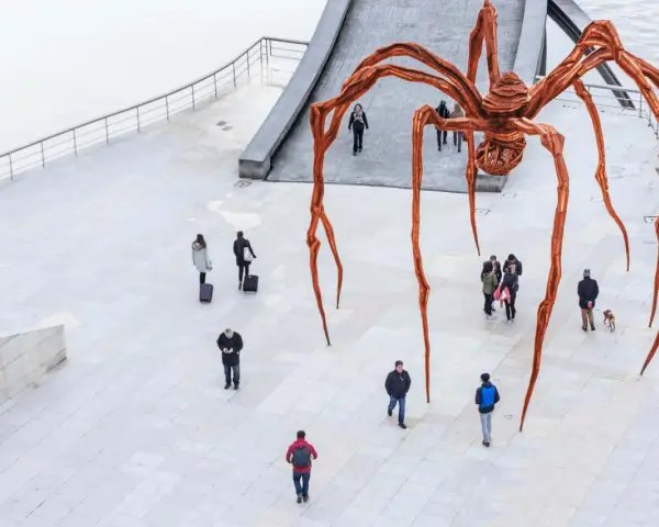 Une immense araignée de bronze, œuvre de Louise Bourgeois, domine une place où quelques passants curieux l'observent.