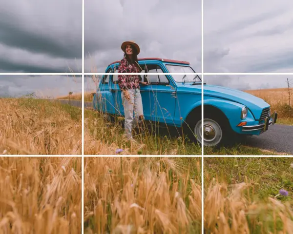 Une femme souriante, chapeau de paille, pose près d'une voiture bleue vintage au milieu d'un champ de blé doré. Photos prises sur le vif.