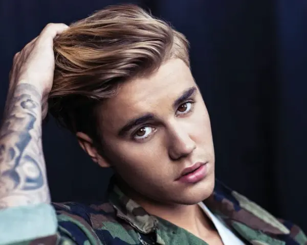 Justin Bieber mit tätowiertem Arm und Camouflage-Jacke, blickt in die Kamera.