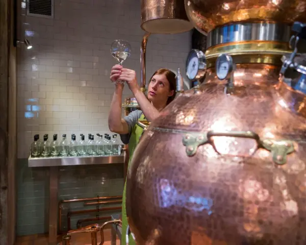 Frau prüft mit einem Glas die Qualität des Destillats. Dies ist ein Schritt, wie wird Gin hergestellt, in einer Kupferbrennerei.