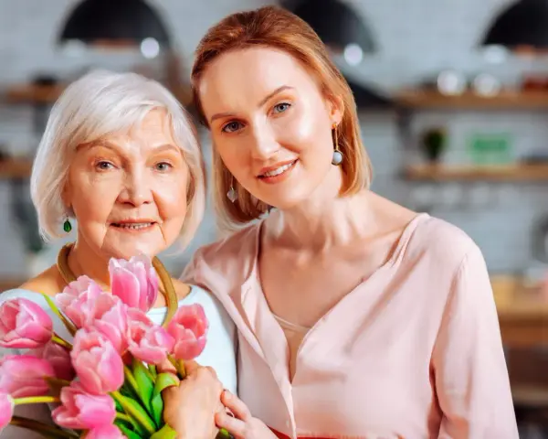 Dwie kobiety, matka i córka, uśmiechają się, trzymając bukiet różowych tulipanów. Wiersz "serce matki" idealnie oddaje ich więź.