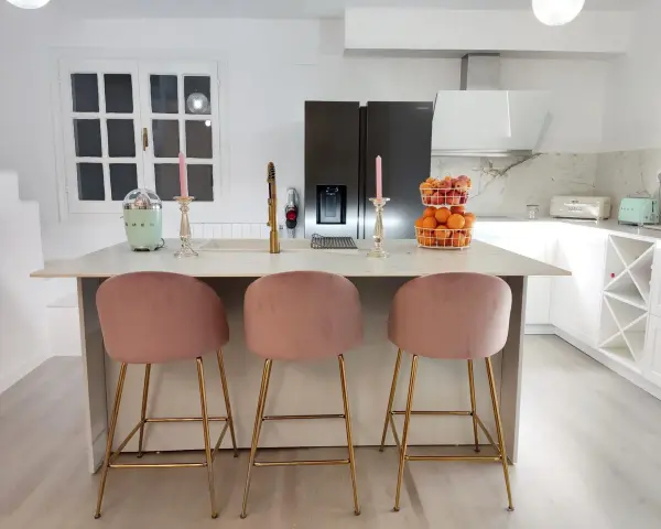 Elegantes cocinas con isla, tres taburetes rosas y dorados invitan a disfrutar.