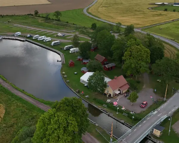 Jonsboda camping vid en kanal med husbilar, båtar och röda stugor. En bro leder över vattnet.