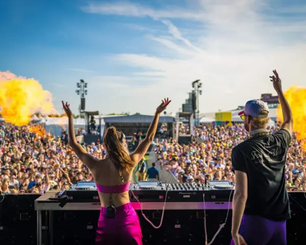 DJ-ka i DJ na scenie, płomienie buchają, tłum szaleje na festiwalu muzyki elektronicznej.