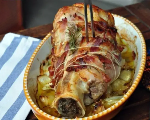 Stinco di vitello al forno, avvolto in pancetta e cotto con cipolle e rosmarino, pronto per essere servito.