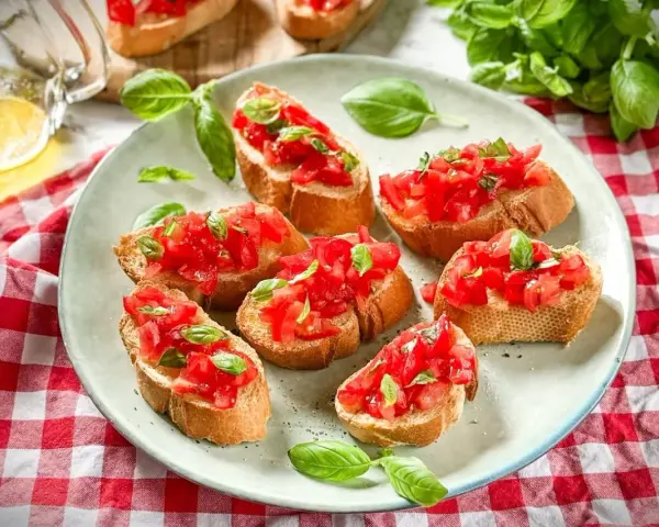 Frische Crostini Variationen mit Tomaten und Basilikum auf einem Teller, garniert mit frischen Basilikumblättern.