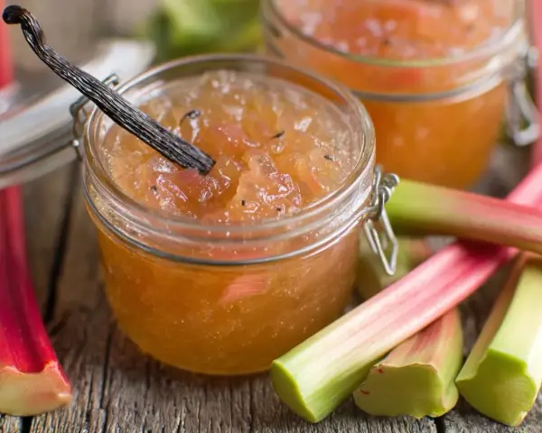 Confiture de rhubarbe maison, avec une gousse de vanille, sur un fond de tiges de rhubarbe fraîches.