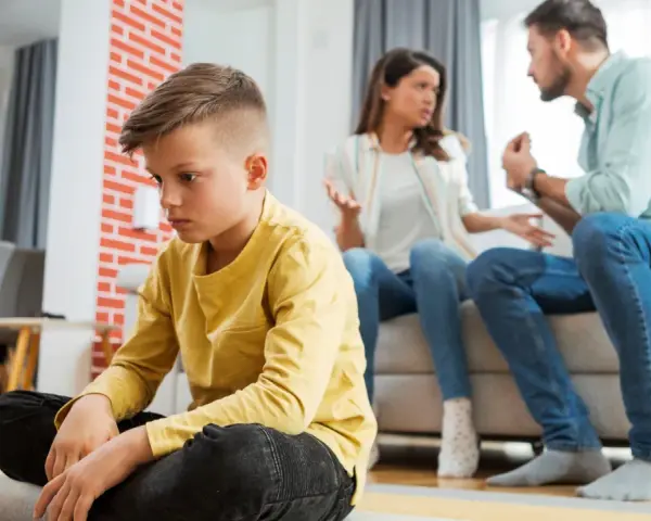 Trauriger Junge sitzt allein, während Eltern streiten. Die Vorteile eines Nebenwohnsitzes für Kinder sind oft, dass sie in einer ruhigeren Umgebung aufwachsen können.