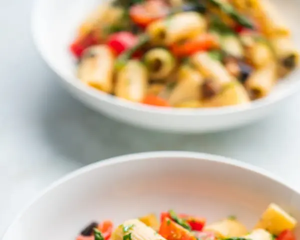Due ciotole bianche piene di pasta con verdure colorate, un piatto estivo invitante.