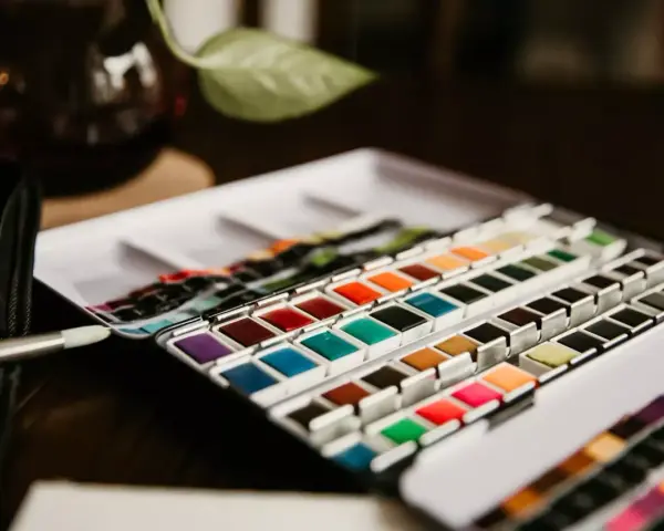 Une palette de matériel peinture aquarelle aux couleurs vives, prête à l'emploi. Un pinceau est posé à côté.