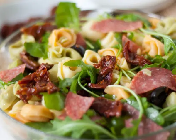 Kolorowa sałatka z tortellini, rukolą, suszonymi pomidorami i salami. Idealna na letni obiad.