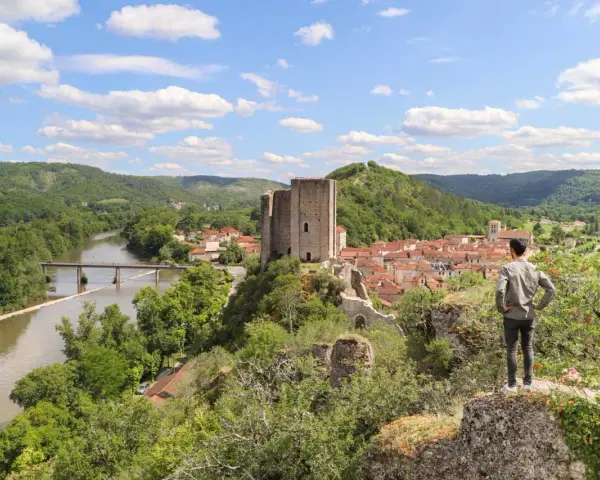 Un homme admire un village médiéval avec un château, un fleuve et des collines verdoyantes, un aperçu du circuit des plus beaux villages du Lot.