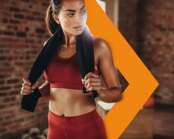 Donna sudata in abbigliamento sportivo rosso, con un asciugamano nero, si riposa dopo l'allenamento. Con il caldo i battiti aumentano, ma lei è determinata.