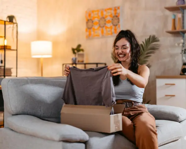 Mujer sonriente desempaqueta una camiseta gris. Espera que las medidas cuerpo sean perfectas.