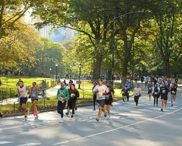 I partecipanti alla maratona di New York corrono lungo un viale alberato in una giornata autunnale, con il sole che filtra tra le foglie dorate.