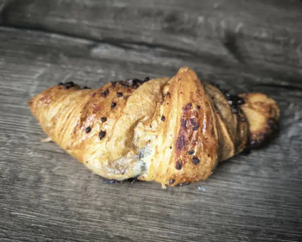 Chrupiący croissant z kawałkami czekolady na drewnianym tle. Idealny na śniadanie, choć warto sprawdzić jego kcal.