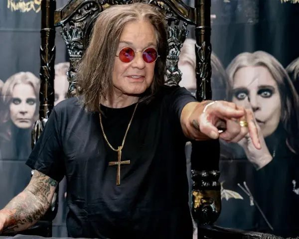 Ozzy Osbourne, geboren 1948, sitzt auf einem Thron und zeigt mit dem Finger. Im Hintergrund sind Bilder von ihm zu sehen.
