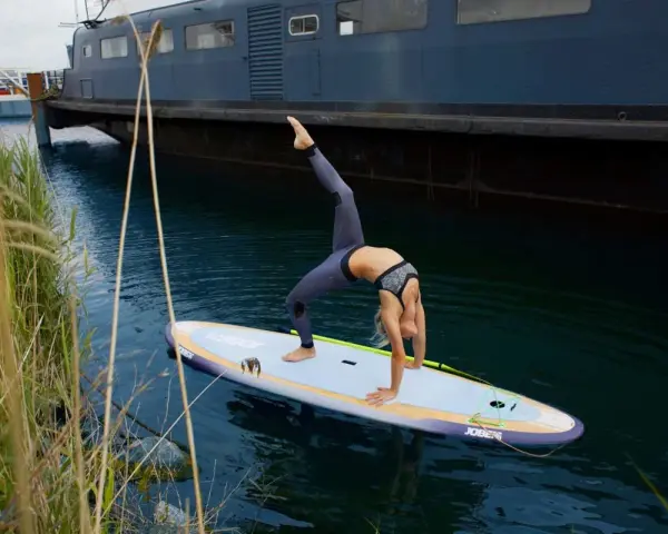 Frau macht Yoga-Brücke auf SUP-Board. Stand up paddle gesund und fördert Balance.