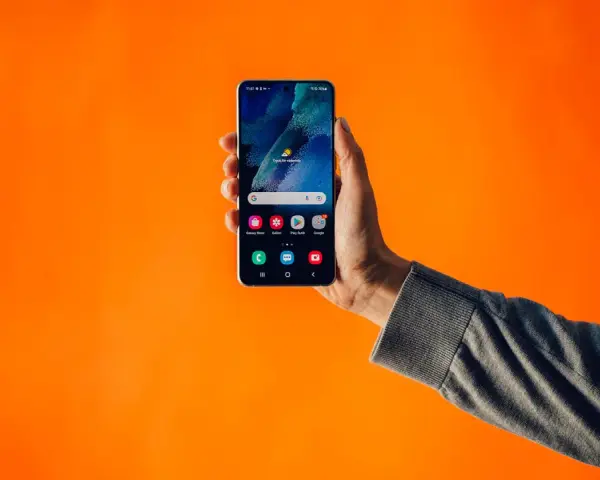 En hand håller upp en smartphone mot en orange bakgrund. Kanske en lösning på problem med dubbla simkort?