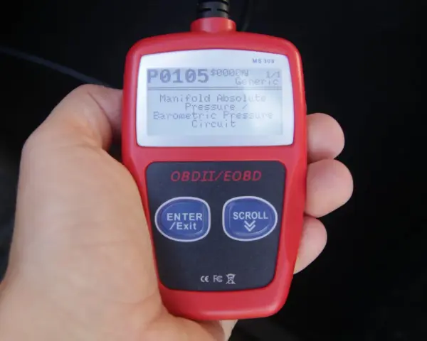 Ręka trzyma czytnik OBD, wyświetlający kod błędu P0105: "Manifold Absolute Pressure / Barometric Pressure Circuit". To jeden z wielu kodów błędów OBD po polsku.