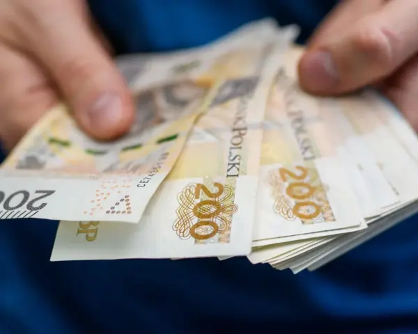 Dłonie trzymające stos banknotów 200 zł. Może to symbolizować zarobki w najlepiej płatnych zawodach.