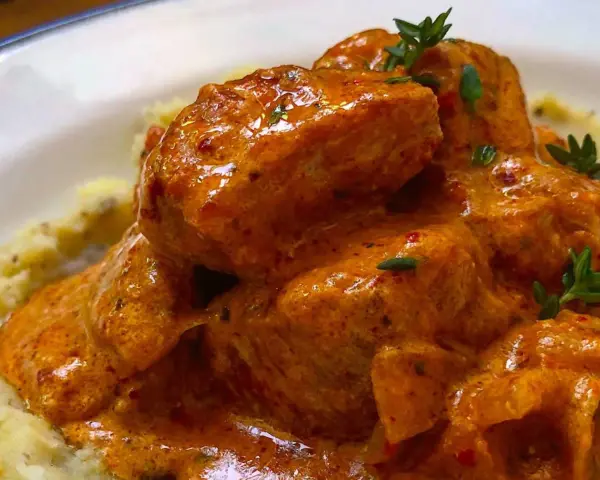 Sabroso pavo en salsa cremosa, adornado con hierbas frescas, servido sobre puré de patatas.