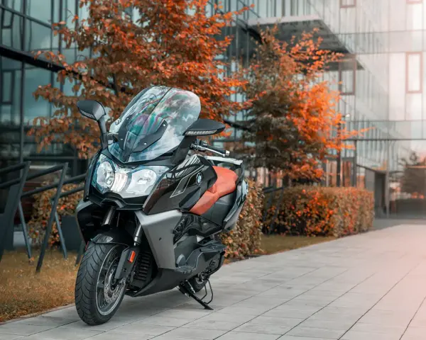 Elegancki skuter BMW C 650 GT z brązową kanapą stoi przed nowoczesnym budynkiem, otoczony jesienną zielenią.