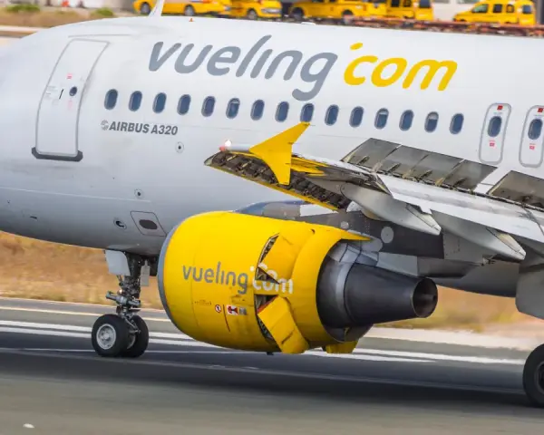 Samolot linii Vueling, hiszpańskie linie lotnicze, z żółtym silnikiem i logo na skrzydle, kołuje po pasie startowym.