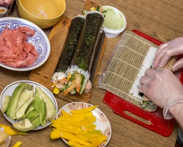 Przygotowanie domowego sushi: ryż, awokado, mango, imbir i rolki w trakcie zwijania.