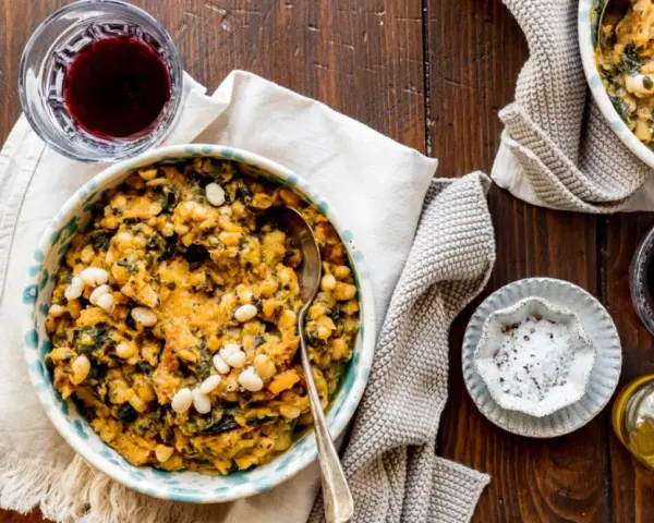 Un piatto di fagioli e verdure, un classico esempio di cose tipiche toscane, accompagnato da vino rosso e olio.
