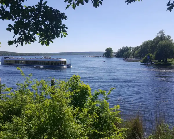Ein Ausflugsboot fährt auf einem glitzernden See bei Potsdam. Grüne Bäume säumen das Ufer, ideal für einen entspannten Tag an den Badeseen Potsdam.