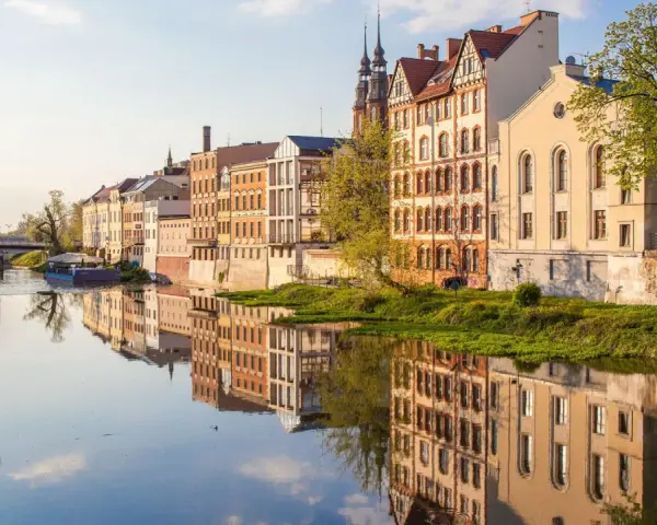 Nad Odrą w Opolu, zabytkowe kamienice odbijają się w wodzie. Spacerując brzegiem, odkryjesz urokliwe zakątki, co można zwiedzić w Opolu.