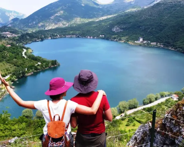 Coppia ammira un lago a forma di cuore, circondato da montagne verdi e alberi.