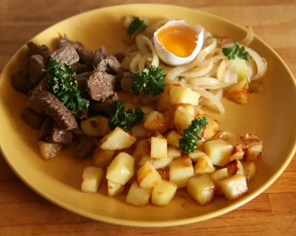 En tallrik med stekt kött, stekt potatis, stekt lök och ett kokt ägg. En klassisk rätt som representerar svenskt mat.