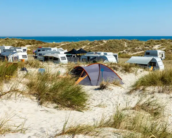 Ein sonniger Campingplatz in Deutschland am Meer. Wohnwagen und Zelte stehen zwischen Dünen und Strandhafer.
