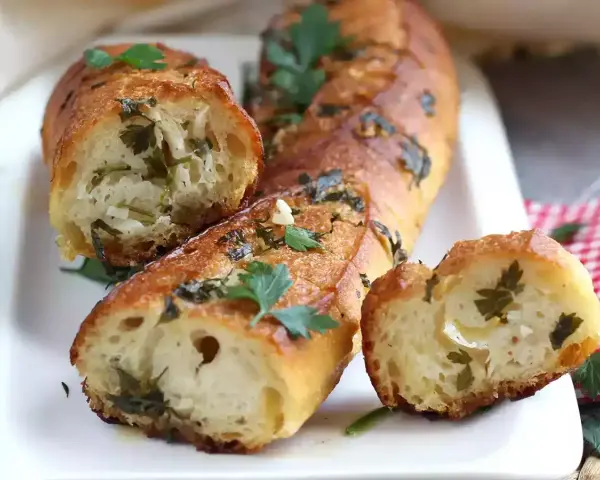 Pan de ajo recién horneado, dorado y crujiente, con trozos de perejil y ajo visibles en su interior.