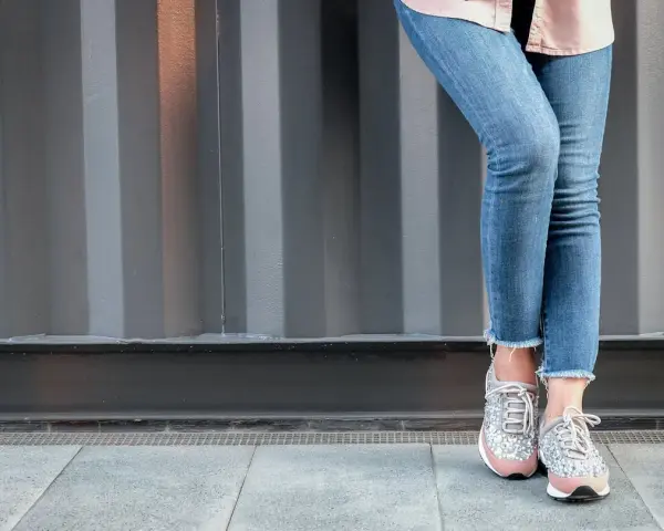 Nogawki jeansów postrzępione na dole, w połączeniu z błyszczącymi sneakersami, tworzą modny look.